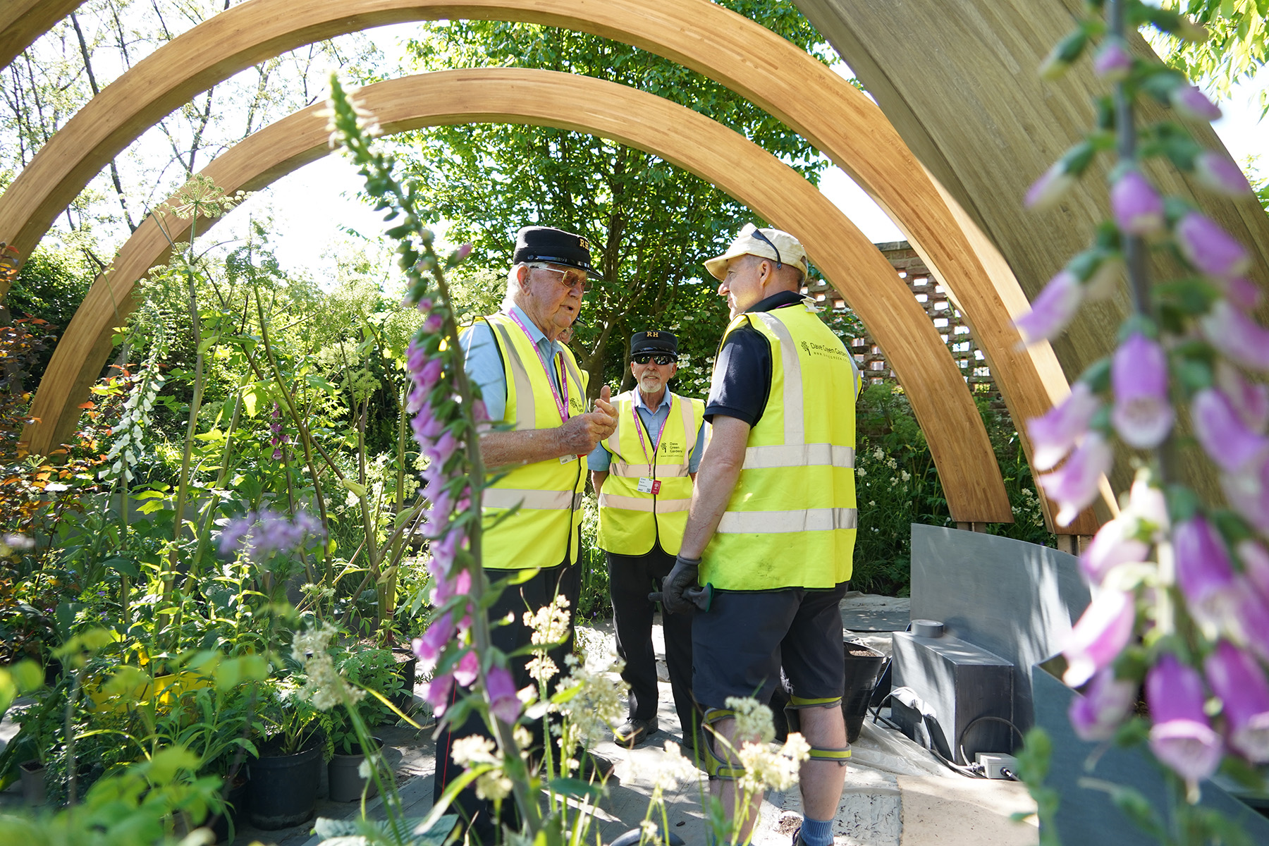Men wearing hi-vis vests speak with a gardener during the Chelsea Flower Show construction