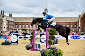 A rider mounted on a horse jumping during competition set amongst the backdrop of Royal Hospital Chelsea