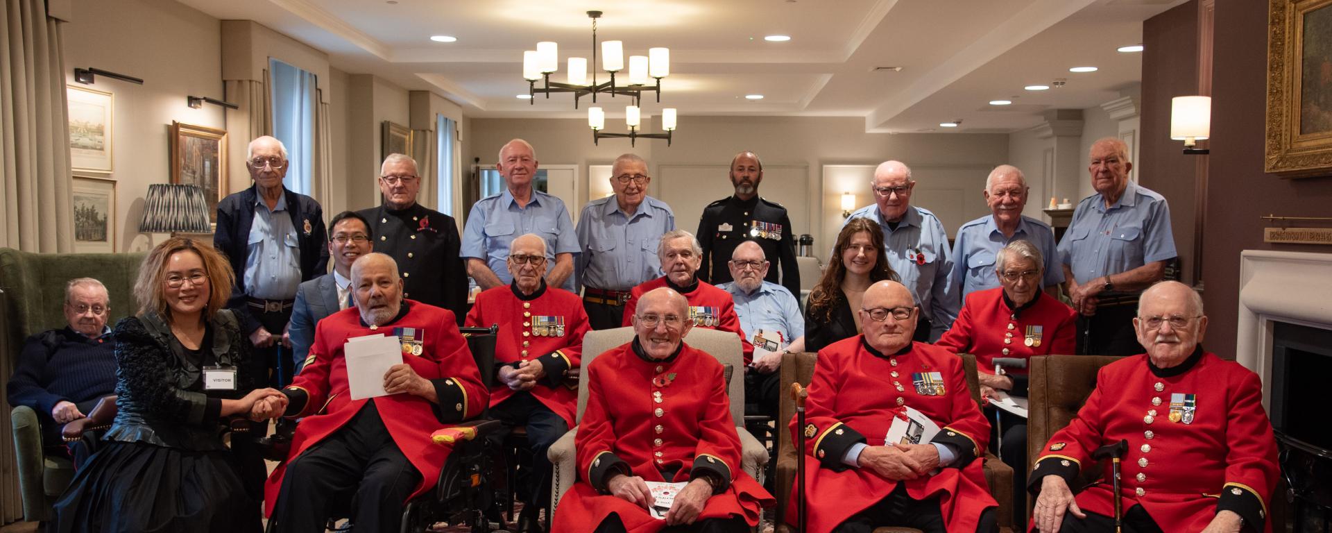 Chelsea Pensioners in scarlet coats and blue uniforms sit in a group with visitors from the North and South Korean community
