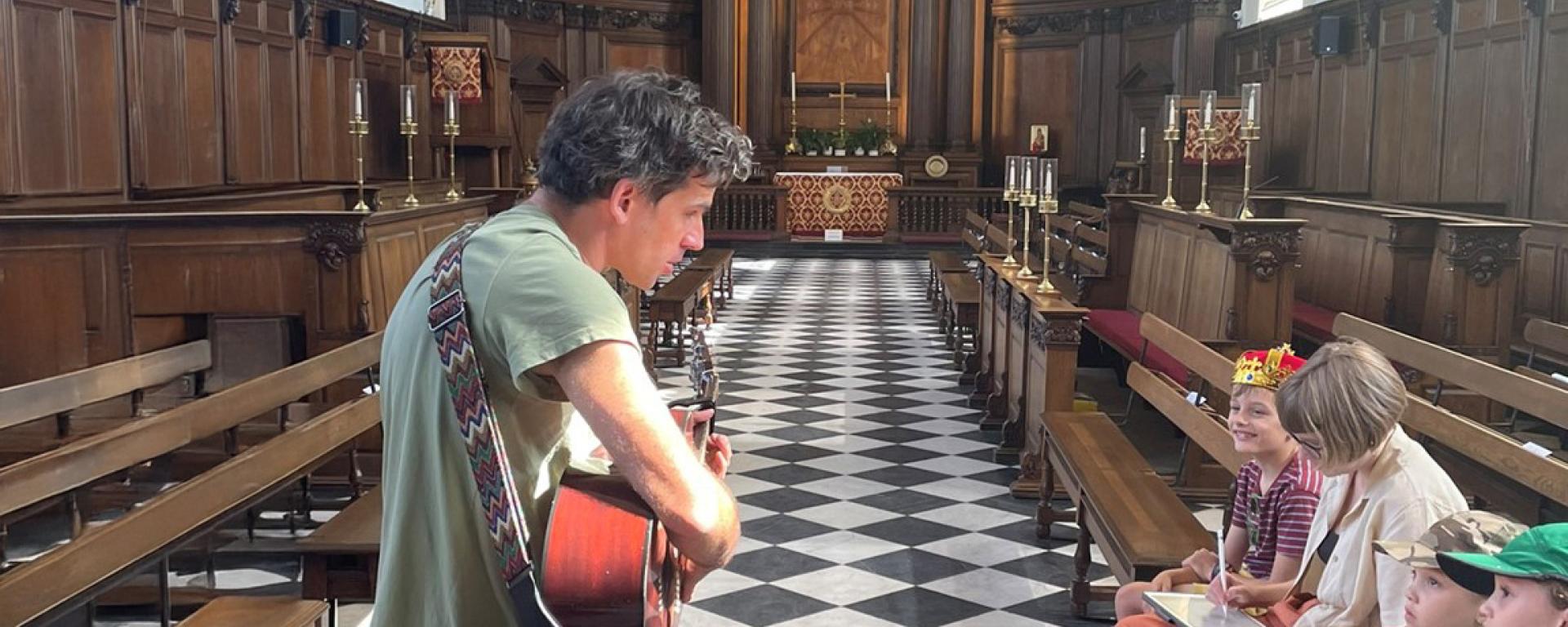 A musician plays his guitar for a family audience in the Wren Chapel at the Royal Hospital Chelsea