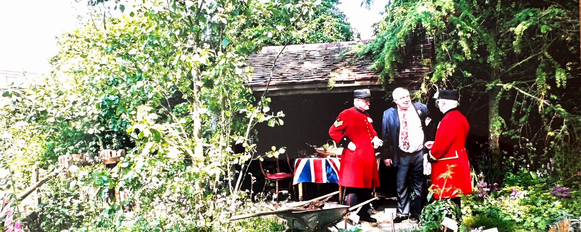 Two Chelsea Pensioners stand with a guest at the Chelsea Flower Show 2005. In the foreground are vegetables grown in the allotment of the show garden "A Soldier's Dream of Blighty"