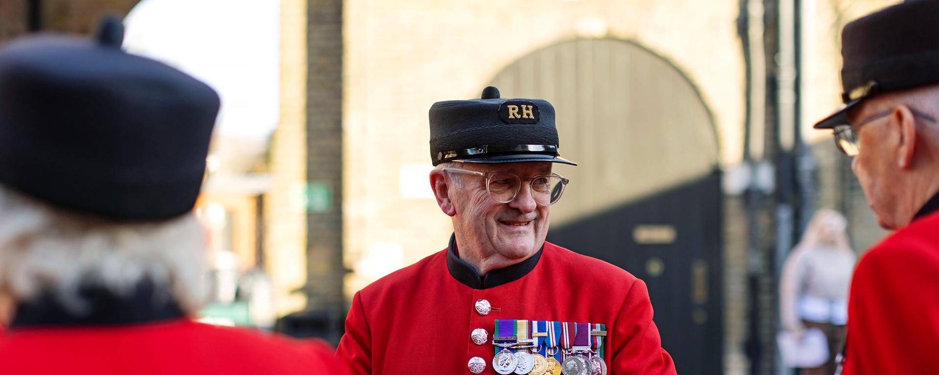 Chelsea Pensioner in a scarlet uniform with medals chatting with fellow residents in the Soane Stable Yard at the Royal Hospital Chelsea.